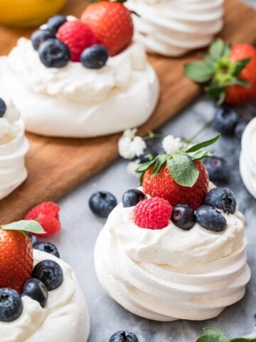 Mini pavlovas topped with whipped cream, strawberries, raspberries, and blueberries.