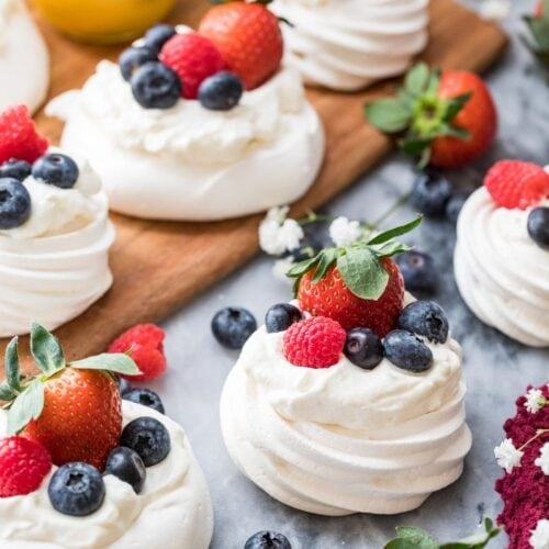 Mini pavlovas topped with whipped cream, strawberries, raspberries, and blueberries.