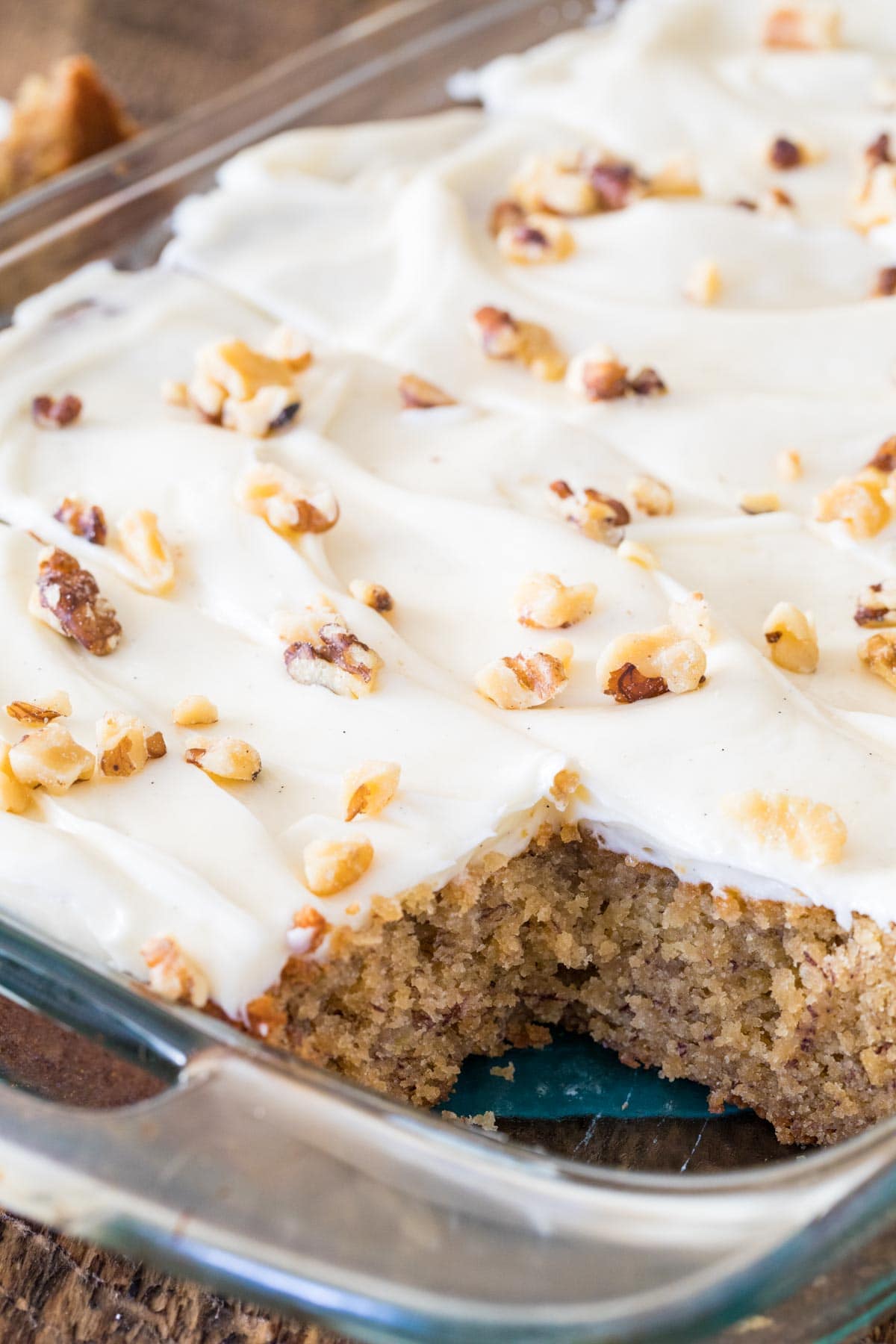 Frosted cake up close topped with chopped walnuts in clear glass baking dish.