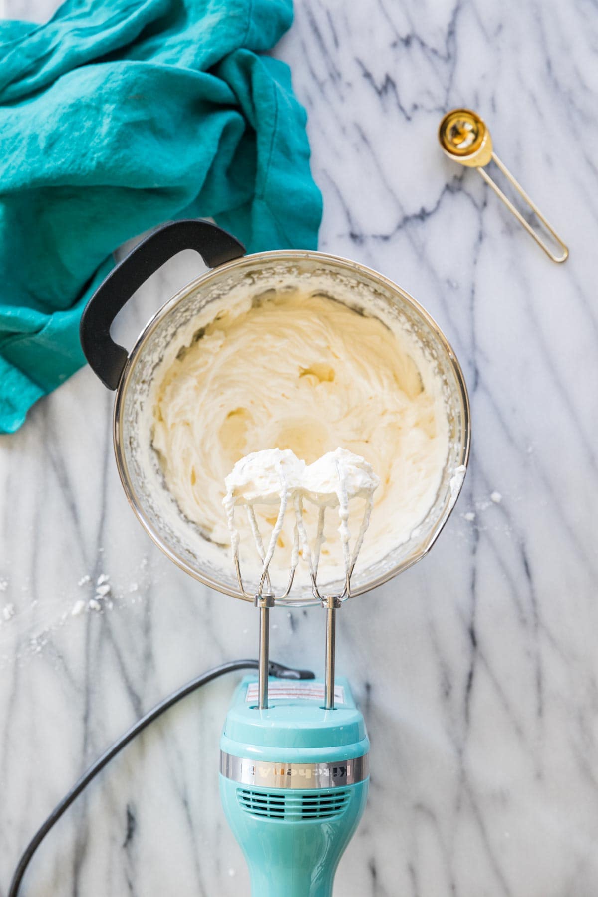 Overhead shot of a metal bowl and electric mixer in the process of making whipped cream.