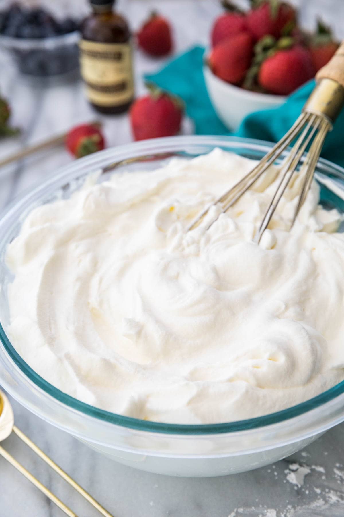 Clear glass mixing bowl filled with billowy whipped cream and a whisk.
