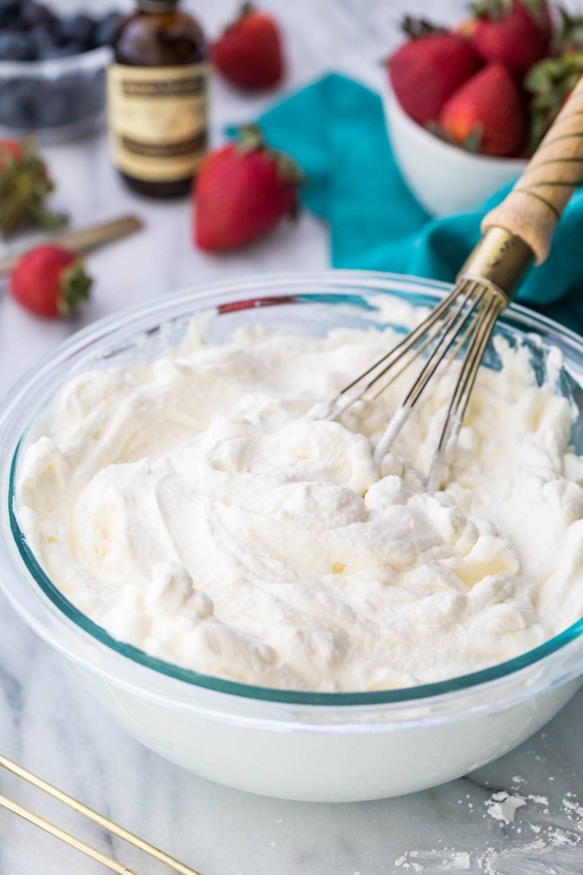 Overhead shot of a clear glass mixing bowl filled with whipped cream and a whisk.