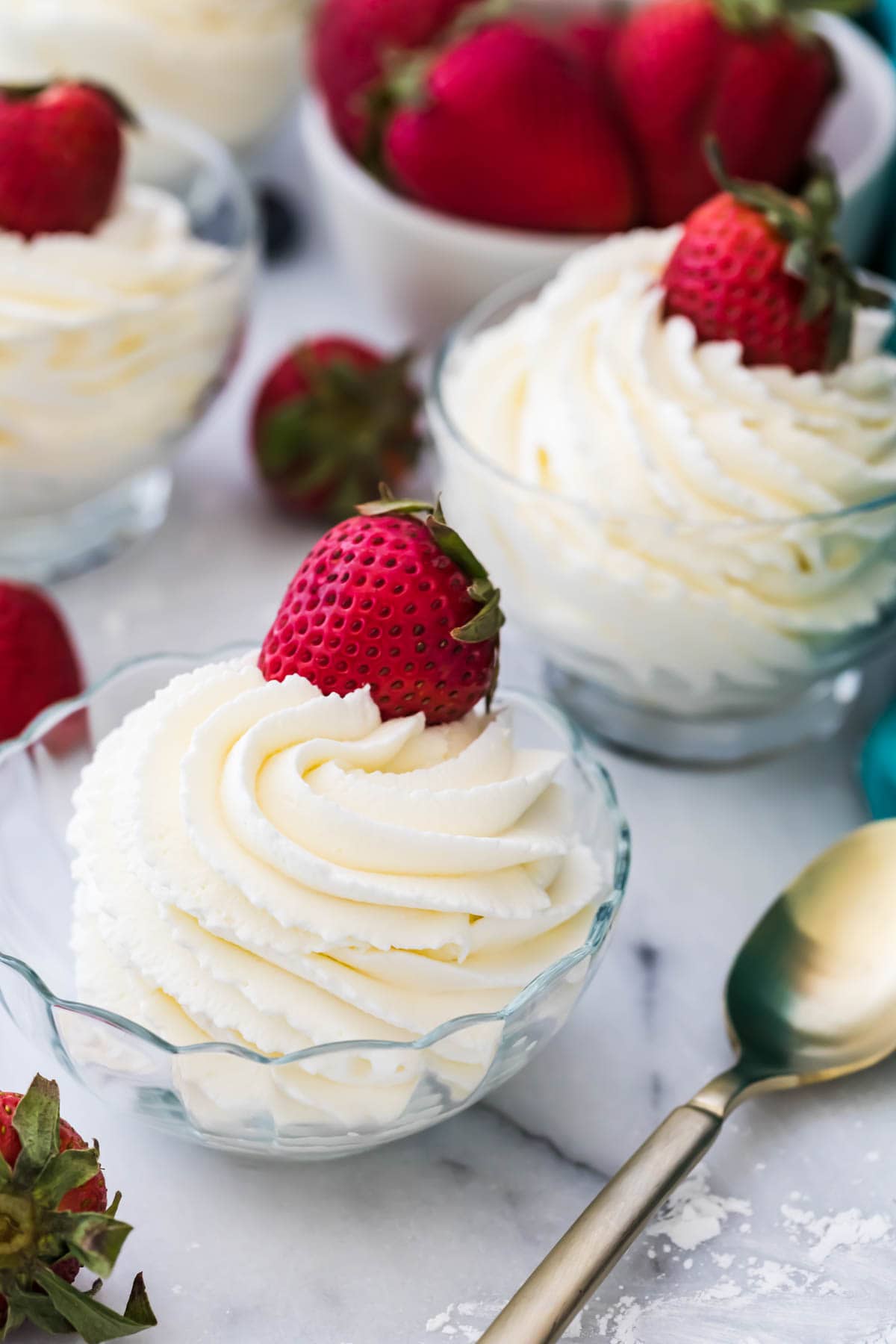 Two clear bowls with whipped cream inside and strawberries on top.