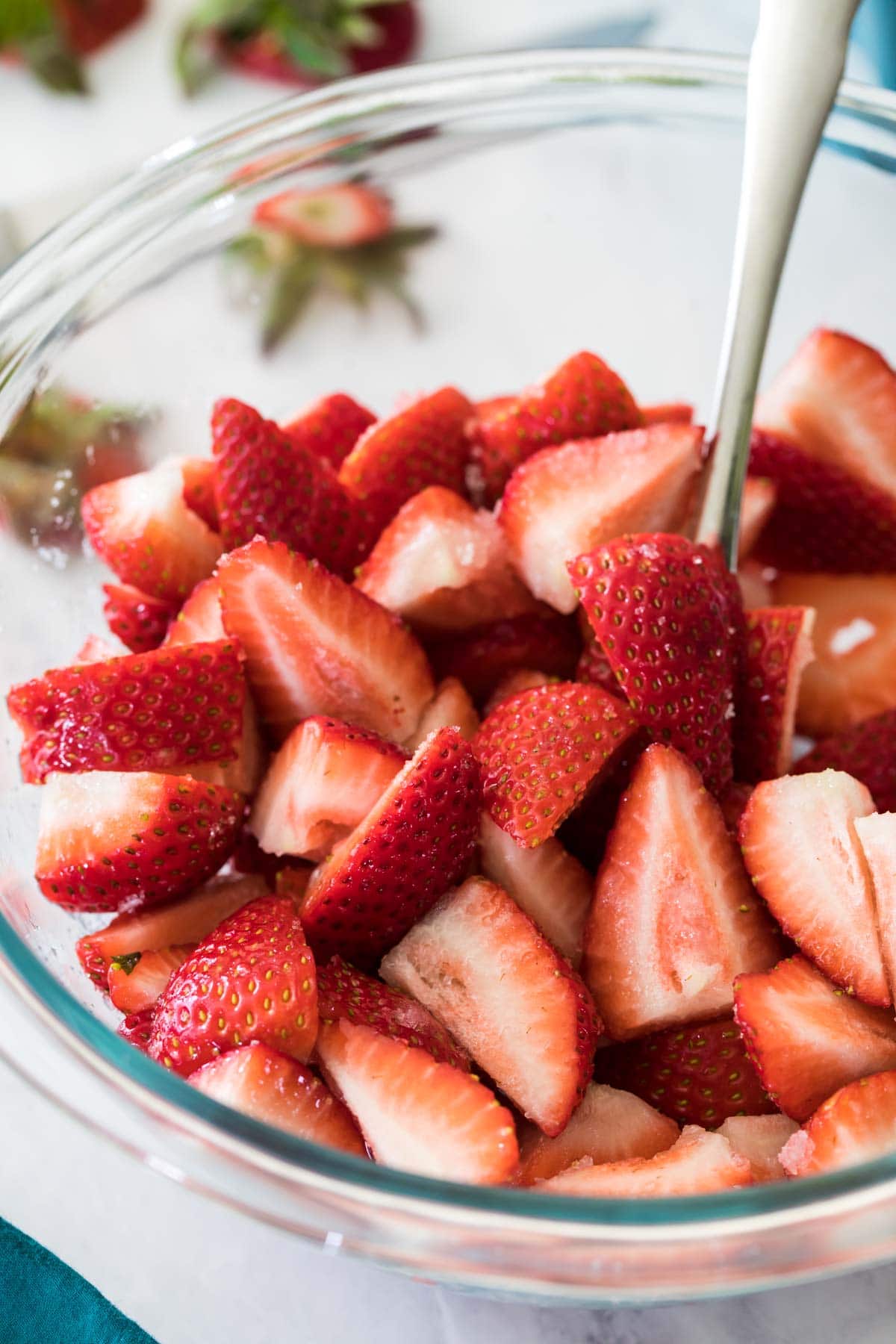 Clear glass mixing bowl filled with cut strawberries.