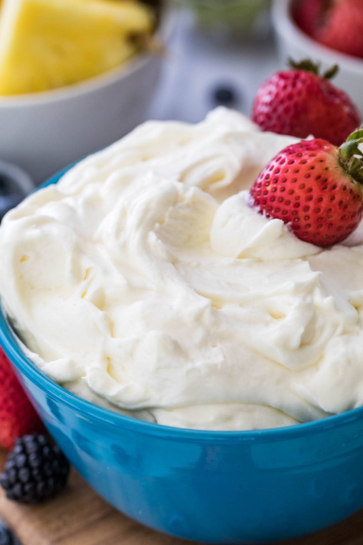 Closeup of fruit dip in blue bowl with strawberries on top.