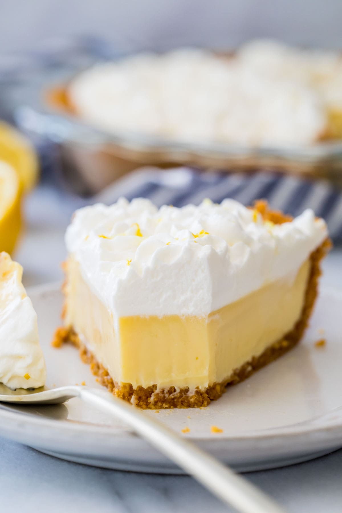 Slice of lemon pie with a bite taken out of it on a white plate.