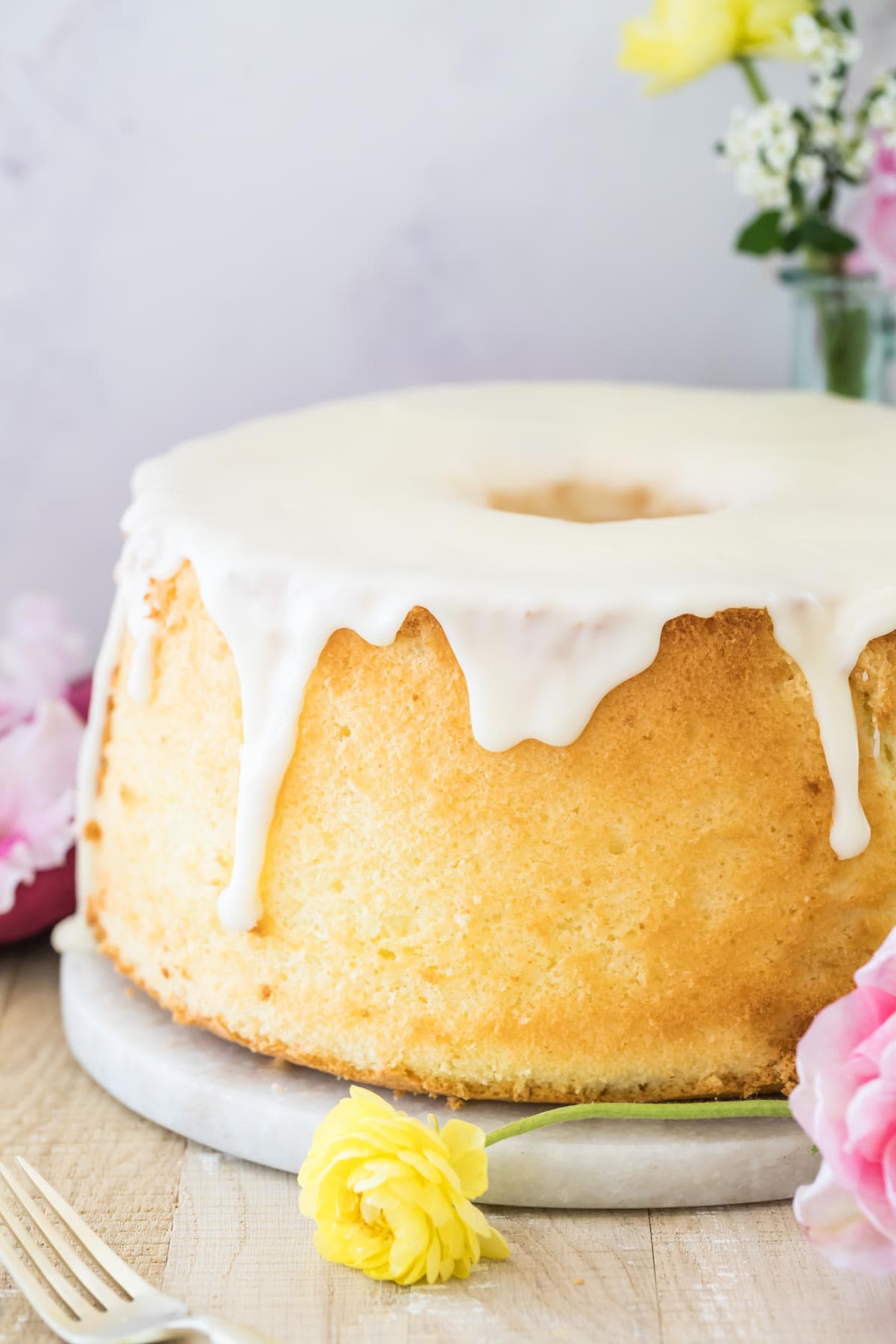 Golden chiffon cake with white glaze surrounded by a pink and yellow flower