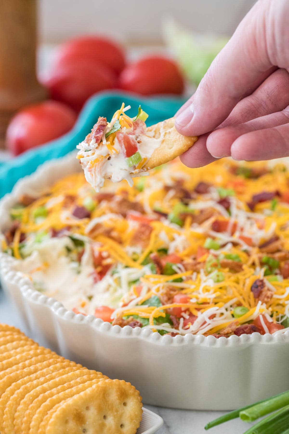 Cracker with blt dip scooped onto it being held in a hand