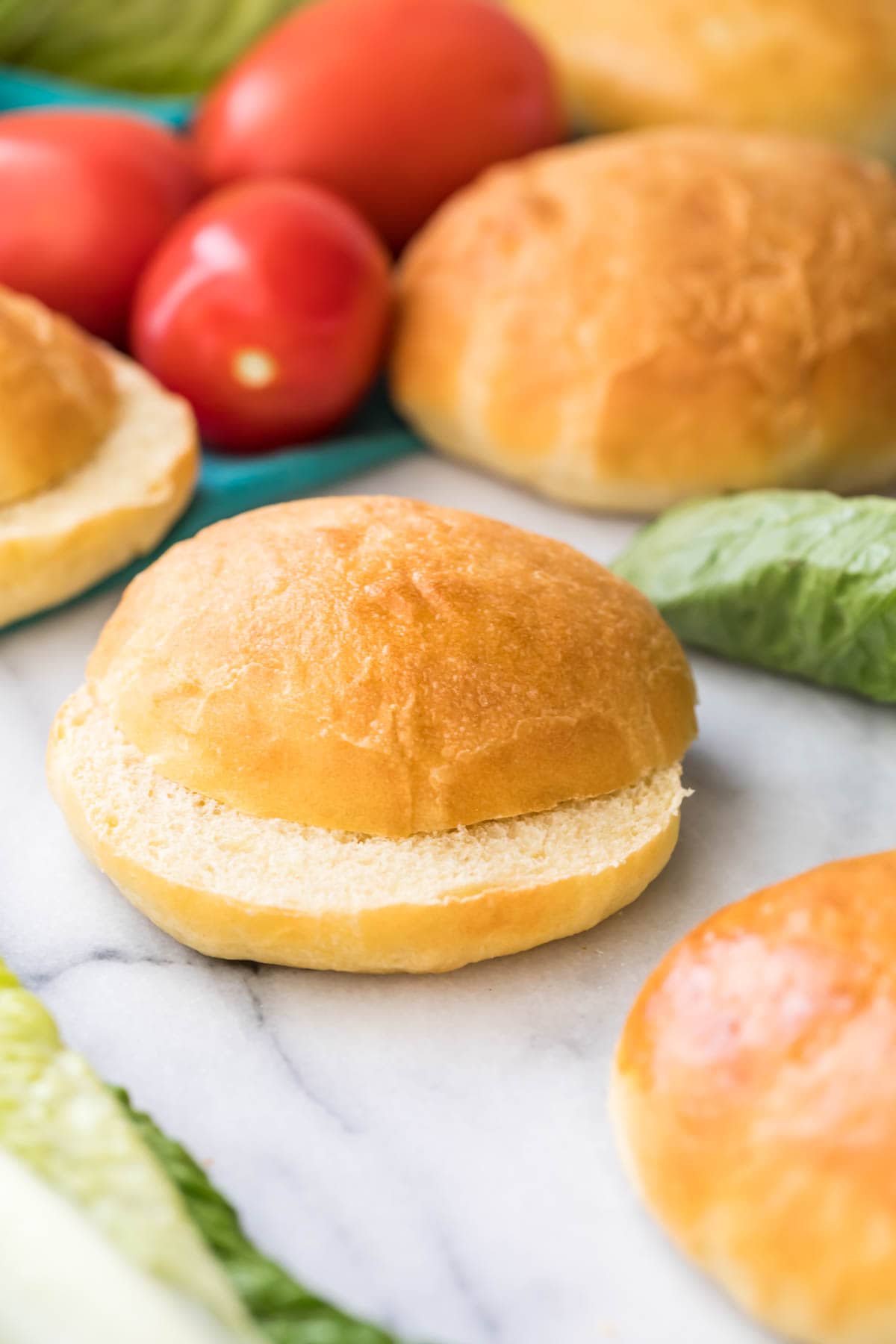 sliced potato bun on marble with lettuce and more buns in background