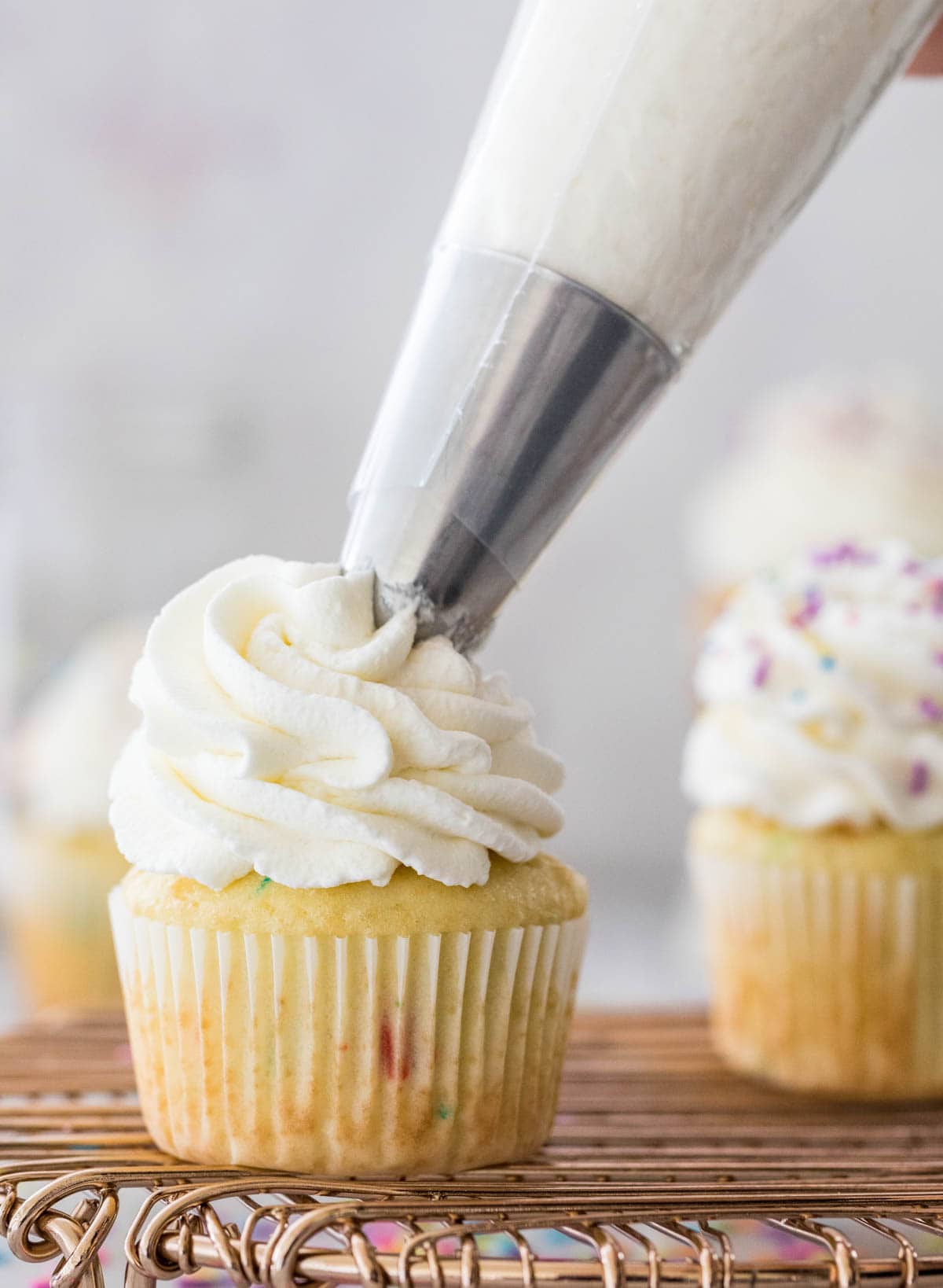 Stabilized whipped cream being piped onto vanilla sprinkle cupcake.