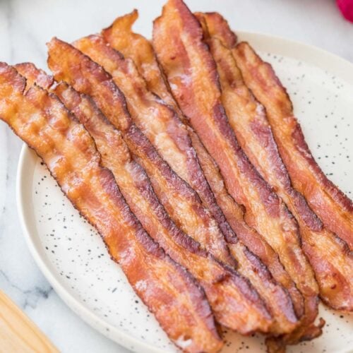 Strips of bacon in the oven on a round speckled white plate