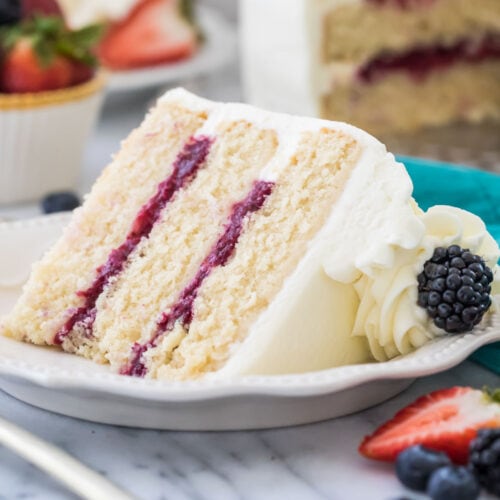 Three layer chantilly cake with berry filling on white plate surrounded by fruit