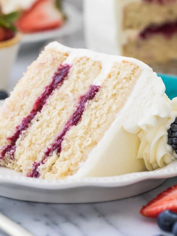 Three layer chantilly cake with berry filling on white plate surrounded by fruit