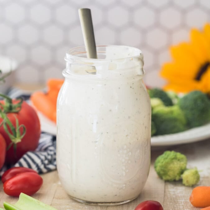 mason jar full of ranch dressing centered in photo with honeycomb tile background and fresh veggies surrounding jar