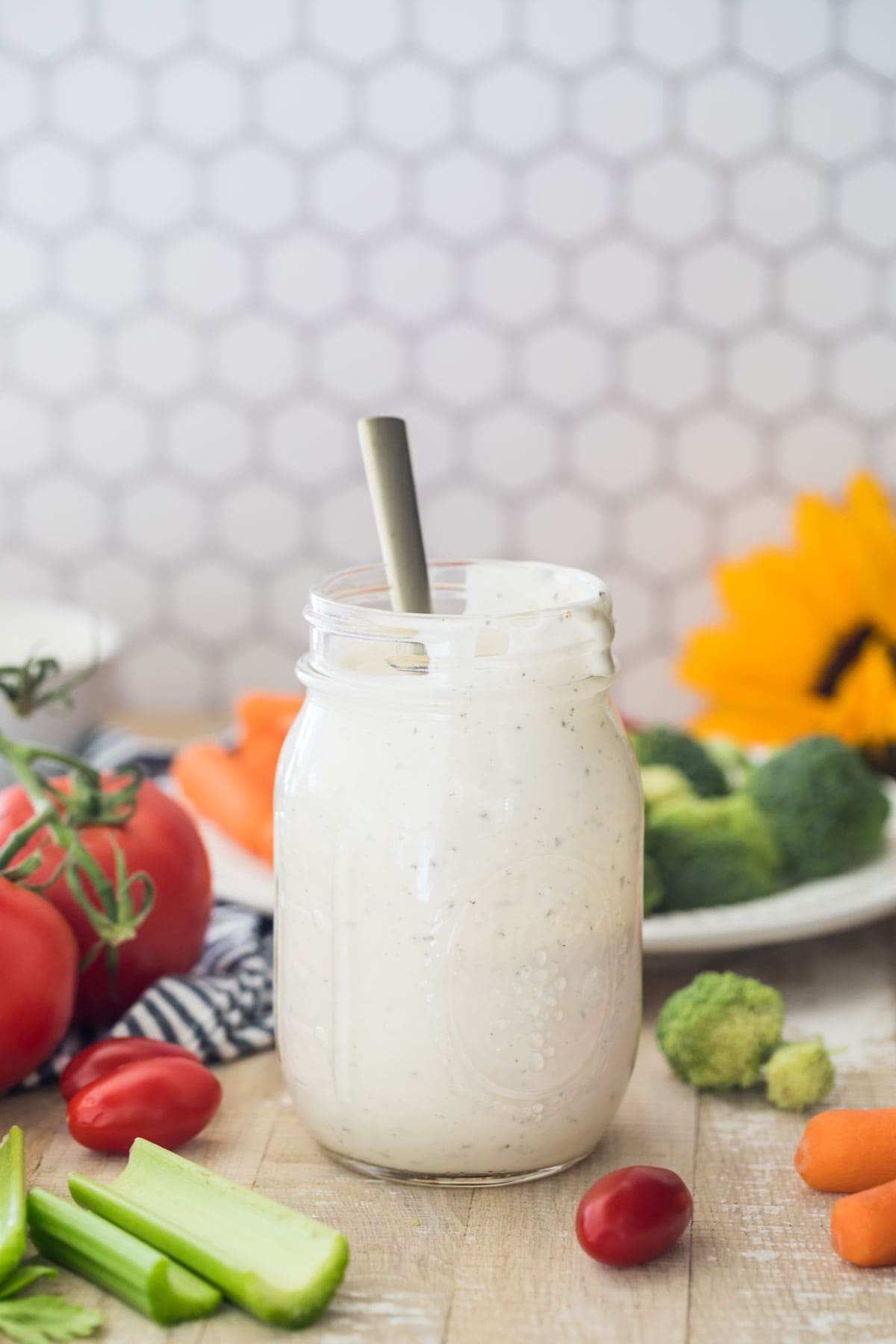 mason jar full of ranch dressing centered in photo with honeycomb tile background and fresh veggies surrounding jar