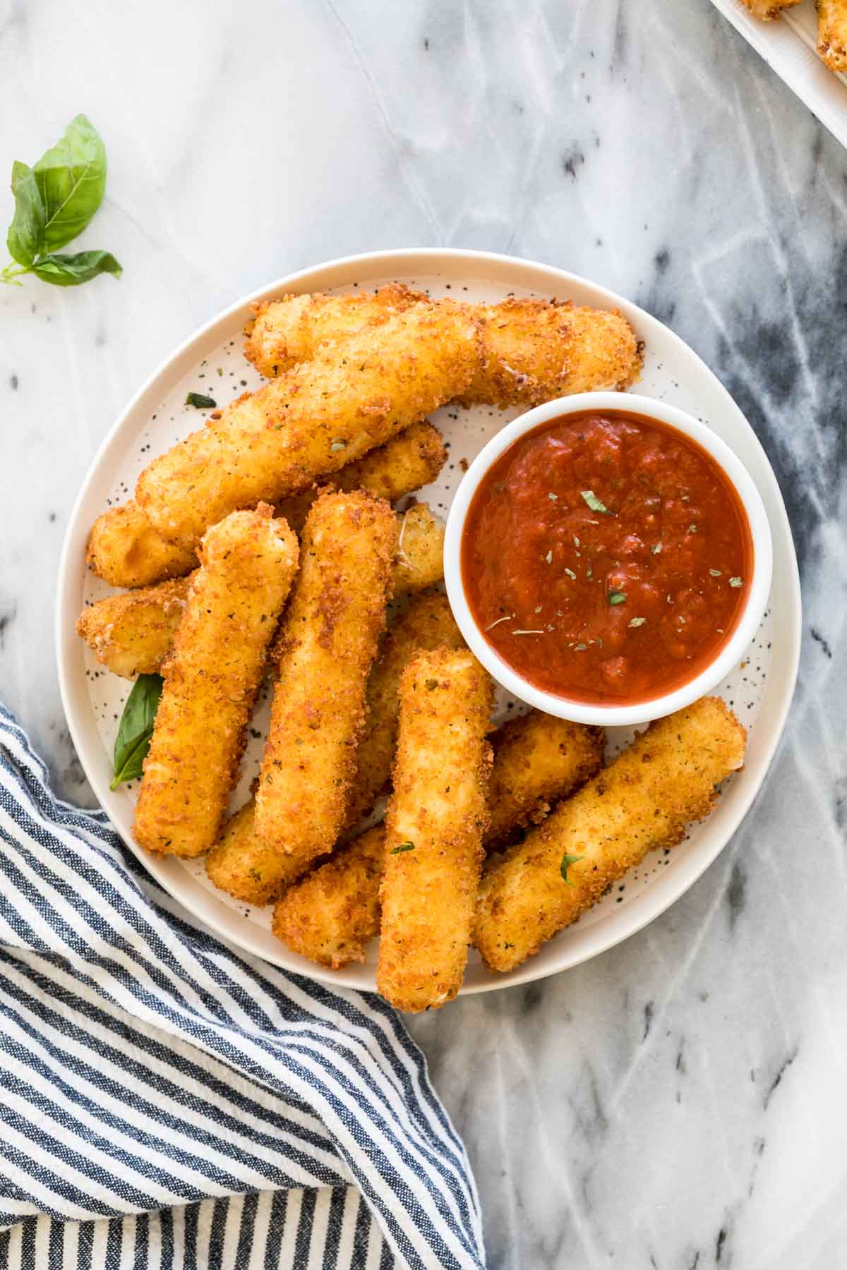 Overhead view of a white plate of breaded and coated mozzarella served with marinara sauce.