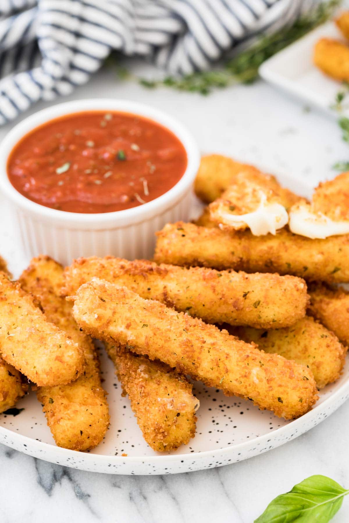 White plate of breaded and coated mozzarella served with marinara sauce.