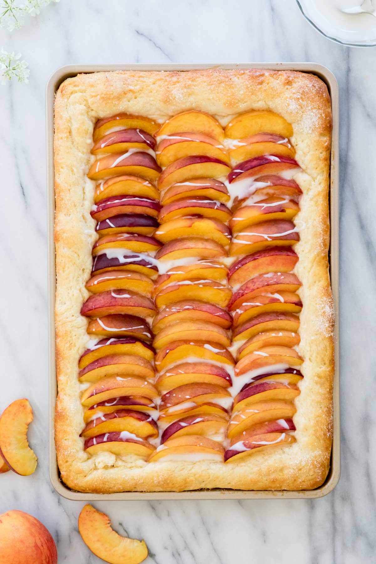 Overhead shot of peach cake in jellyroll pan topped with fresh sliced peaches