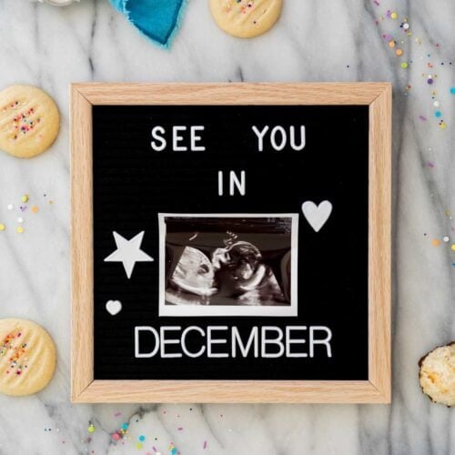 Felt board that reads: "See you in December" with an ultrasound photo in the center. Board is on white marble surrounded by cookies and sprinkles