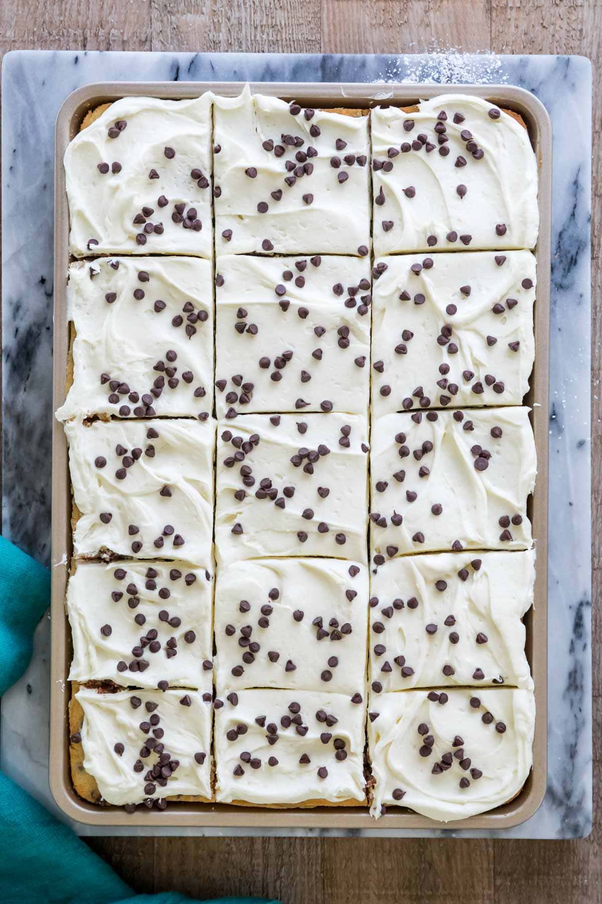 Overhead view of chocolate chip sheet cake baked in a gold jelly roll pan. Iced with white frosting and topped with chocolate chips