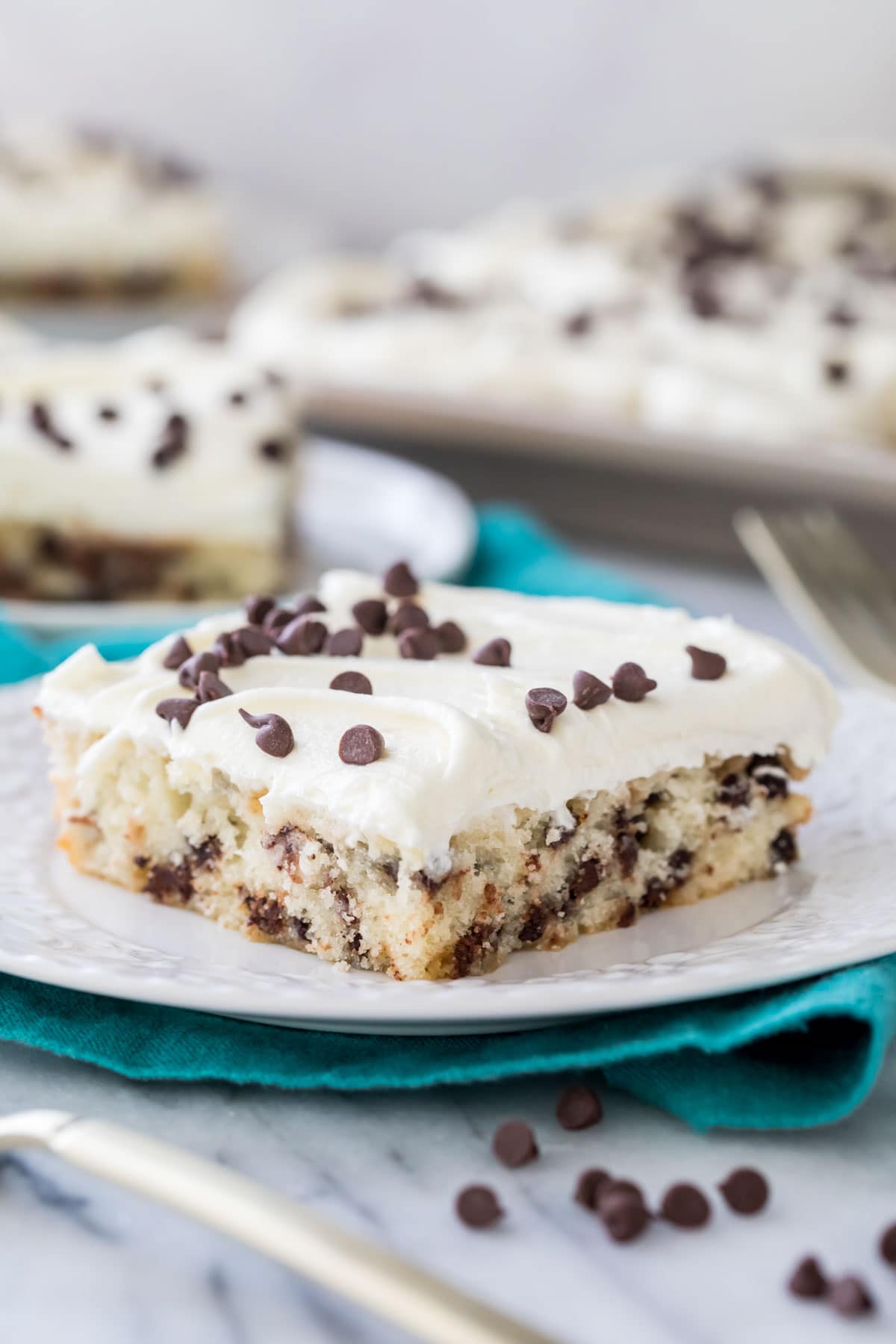 Square slice of chocolate chip sheet cake on a white plate. Frosted with white frosting and mini chocolate chips