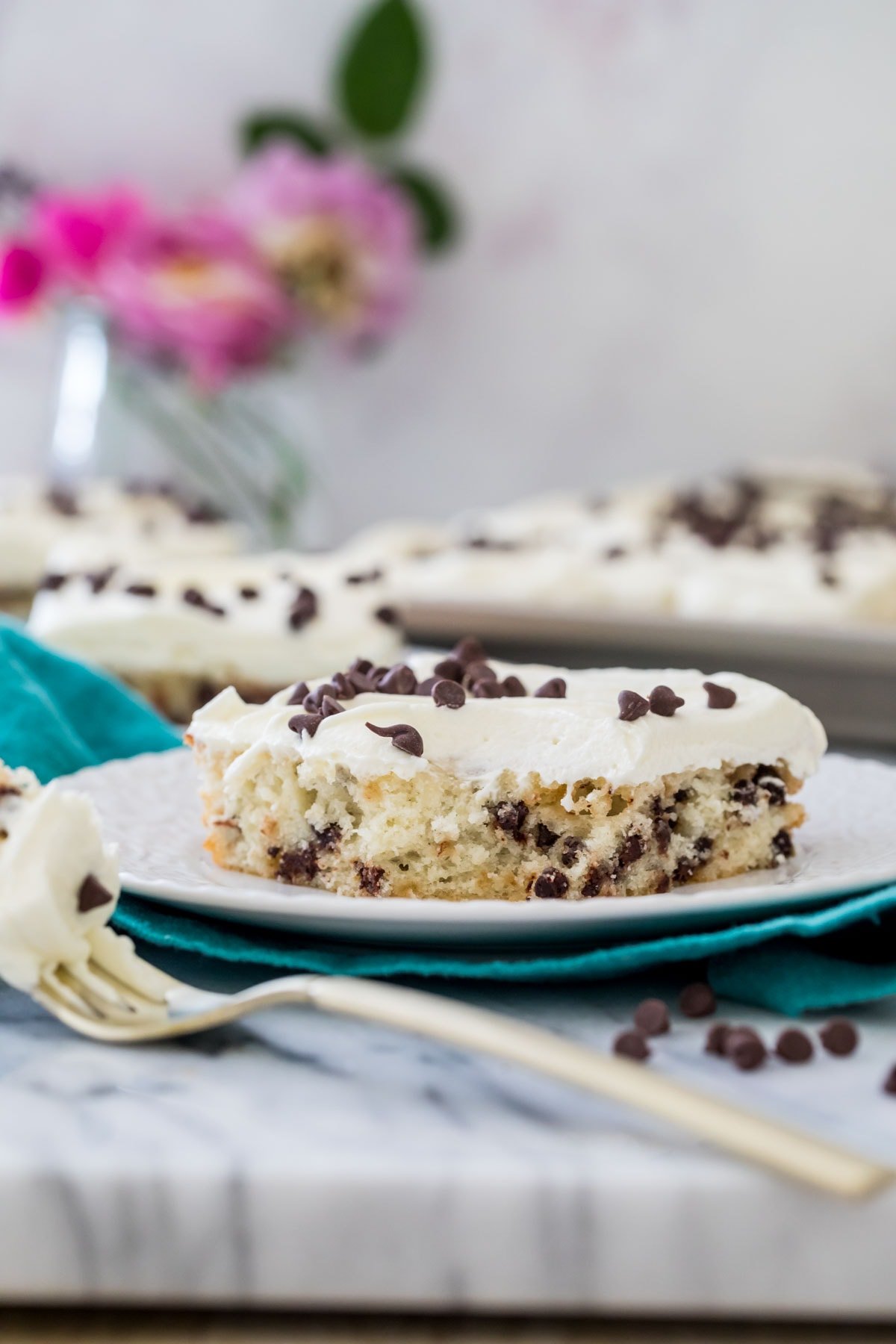 slice of chocolate chip sheet cake on a white plate on a teal towel