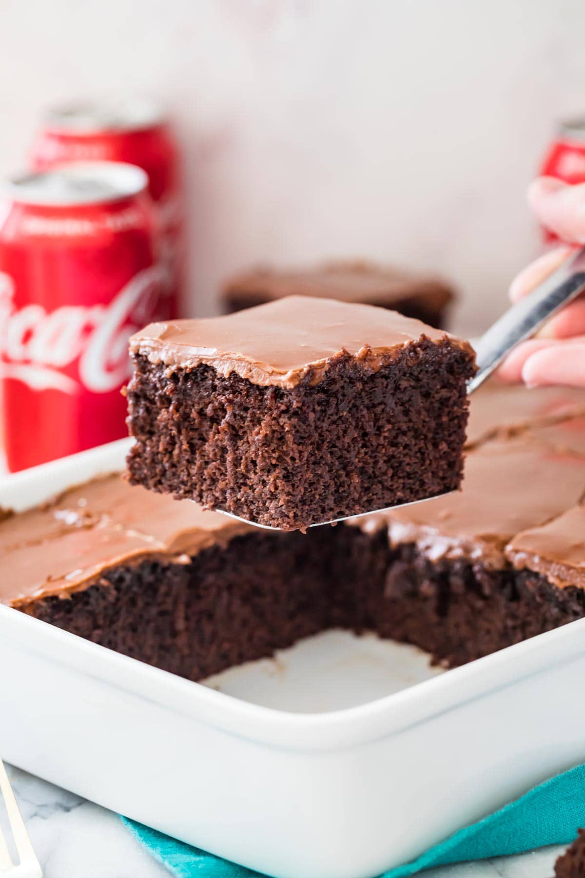 Square slice of frosted coca cola cake being lifted out of cake pan