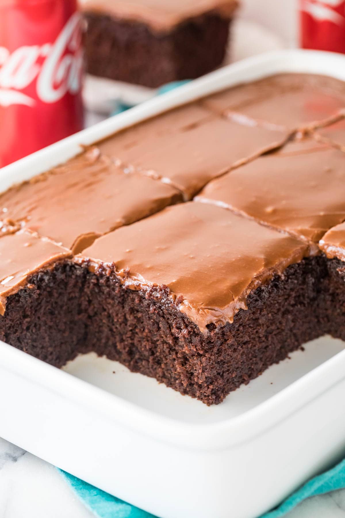 thick-squares-of-coca-cola-cake-with-shiny-brown-frosting-in-white-cake-pan