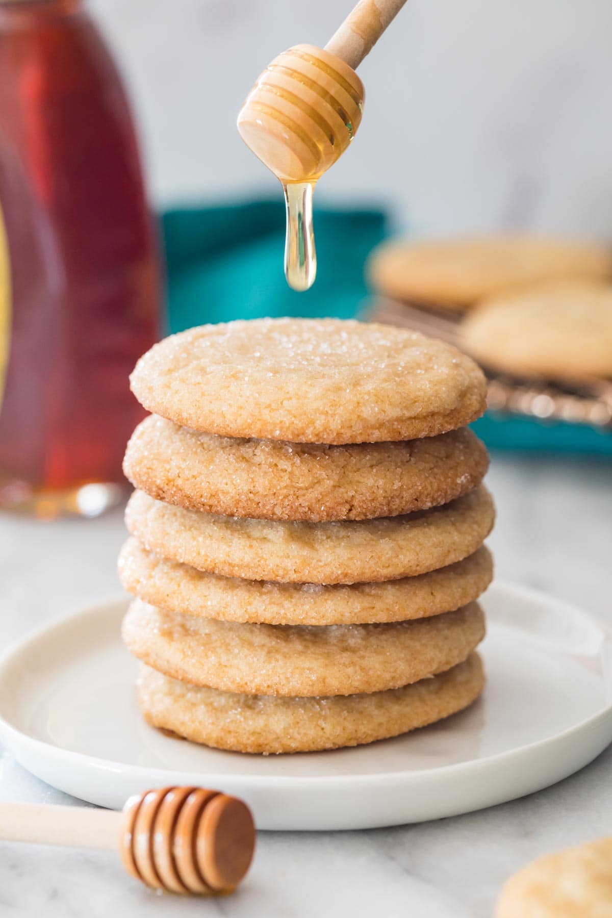 drizzling honey over a stack of honey cookies on white plate