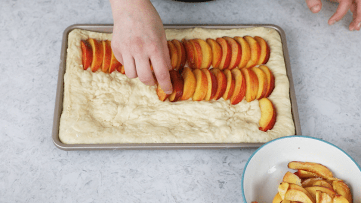 Top-down view of peaches being arranged on peach cake