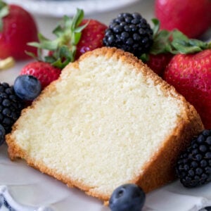 A slice of moist, buttery pound cake surrounded by fresh berries on a white plate