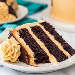 slice of three-layer chocolate cake with peanut butter icing and chocolate ganache with one bite missing on white plate