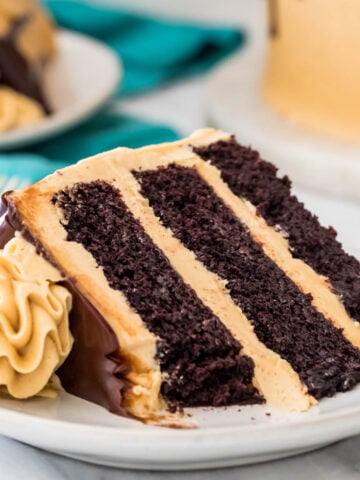 slice of three-layer chocolate cake with peanut butter icing and chocolate ganache with one bite missing on white plate