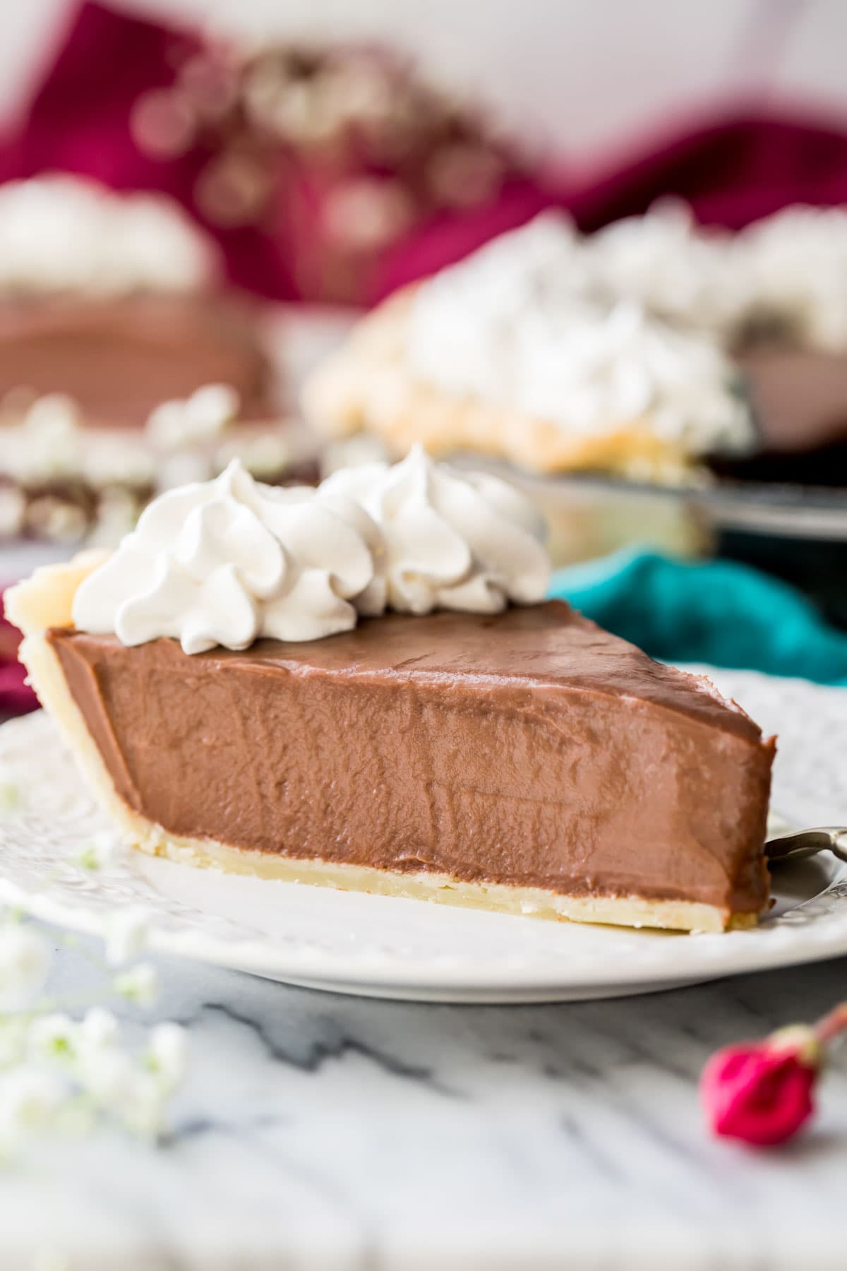 side view of silky smooth chocolate pie topped with whipped cream sitting on white plate