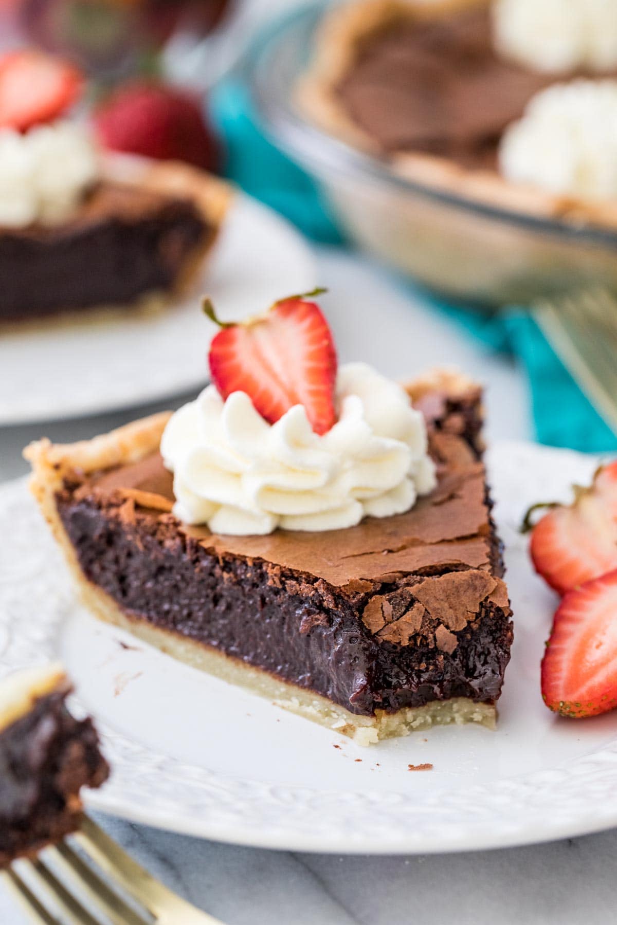 slice of chocolate chess pie topped with whipped cream and a strawberry with one bite missing