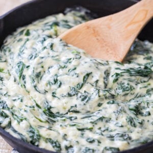 wooden spoon stirring thick and creamy creamed spinach