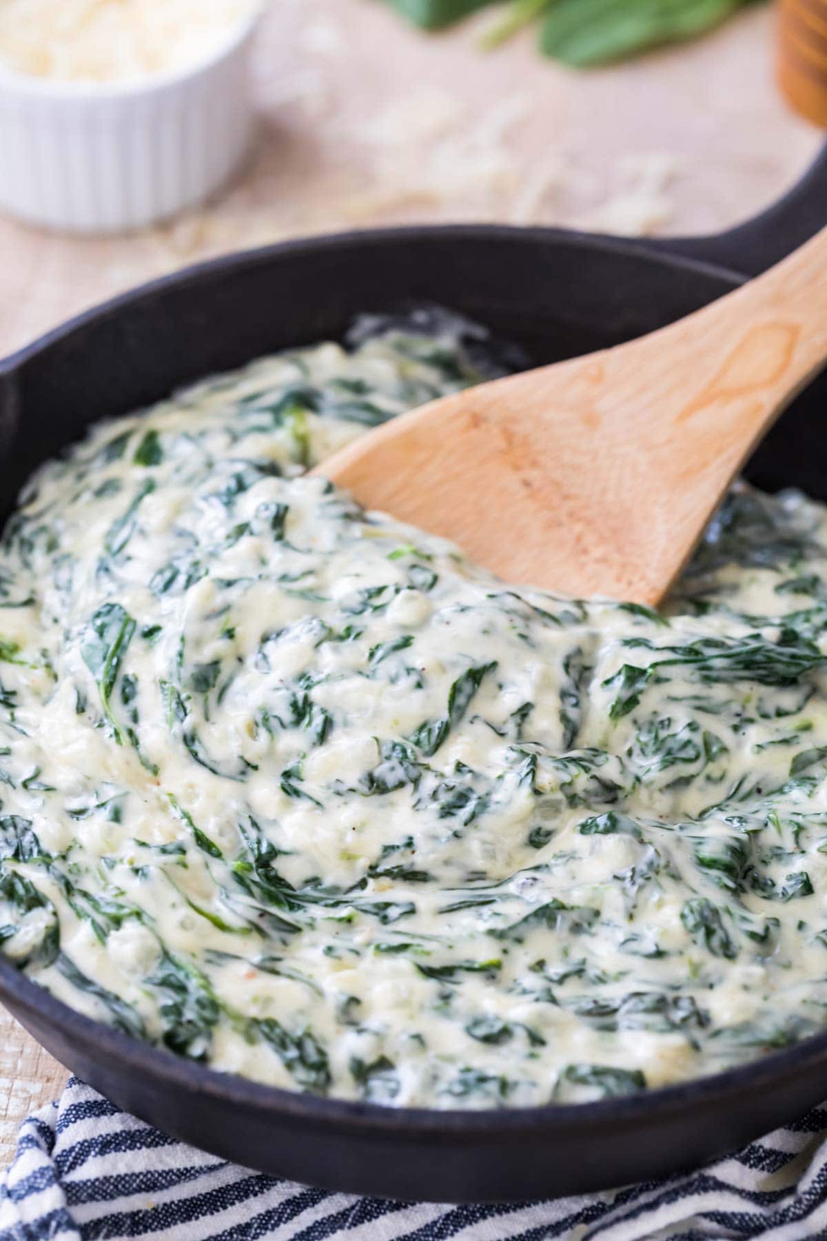 wooden spoon stirring thick and creamy creamed spinach