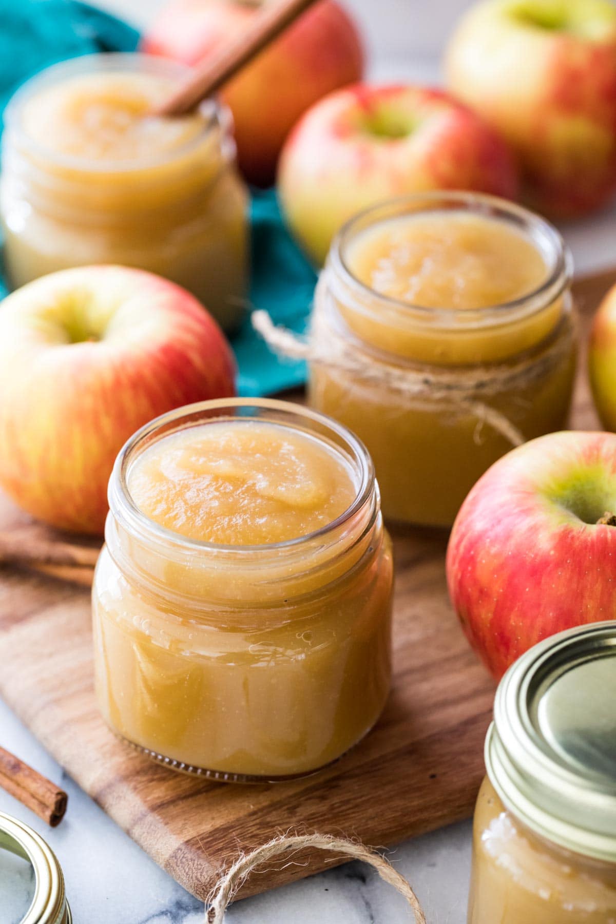 Several glass jars of homemade applesauce surrounded by red honeycrisp apples