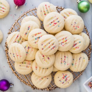 pile of whipped shortbread cookies with sprinkles on gold cooling rack