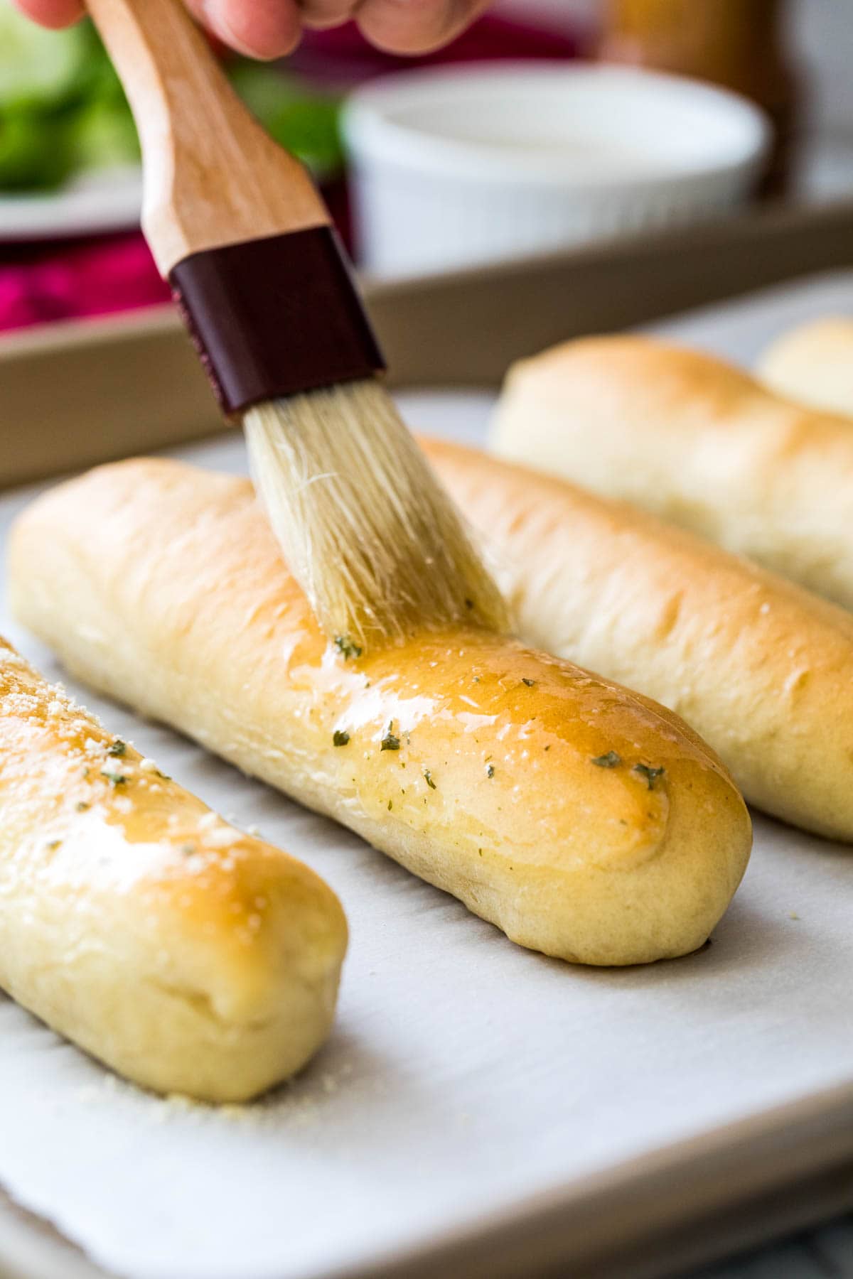 homemade breadsticks being brushed with garlic butter