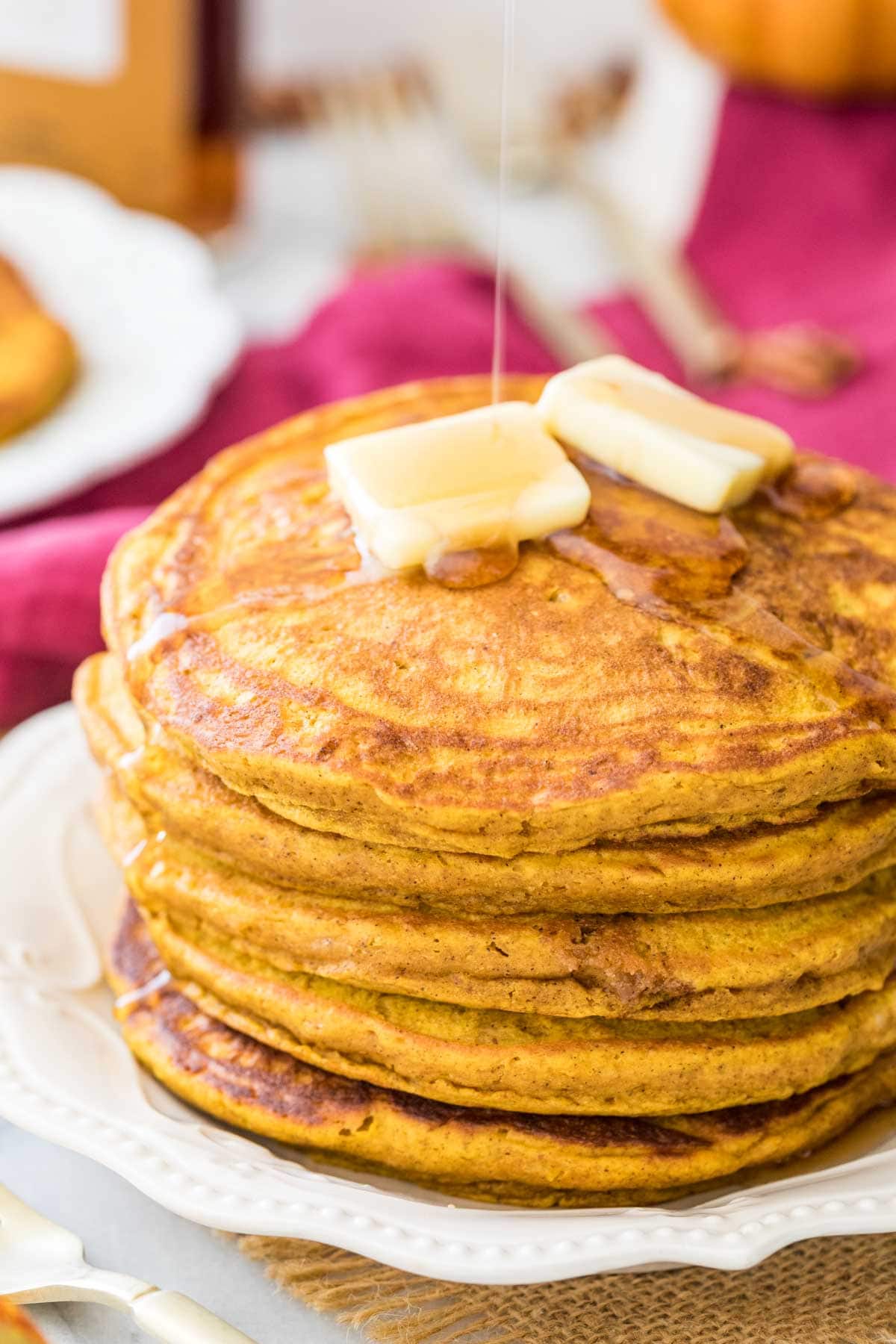 thick, fluffy pumpkin pancakes being drizzled with maple syrup