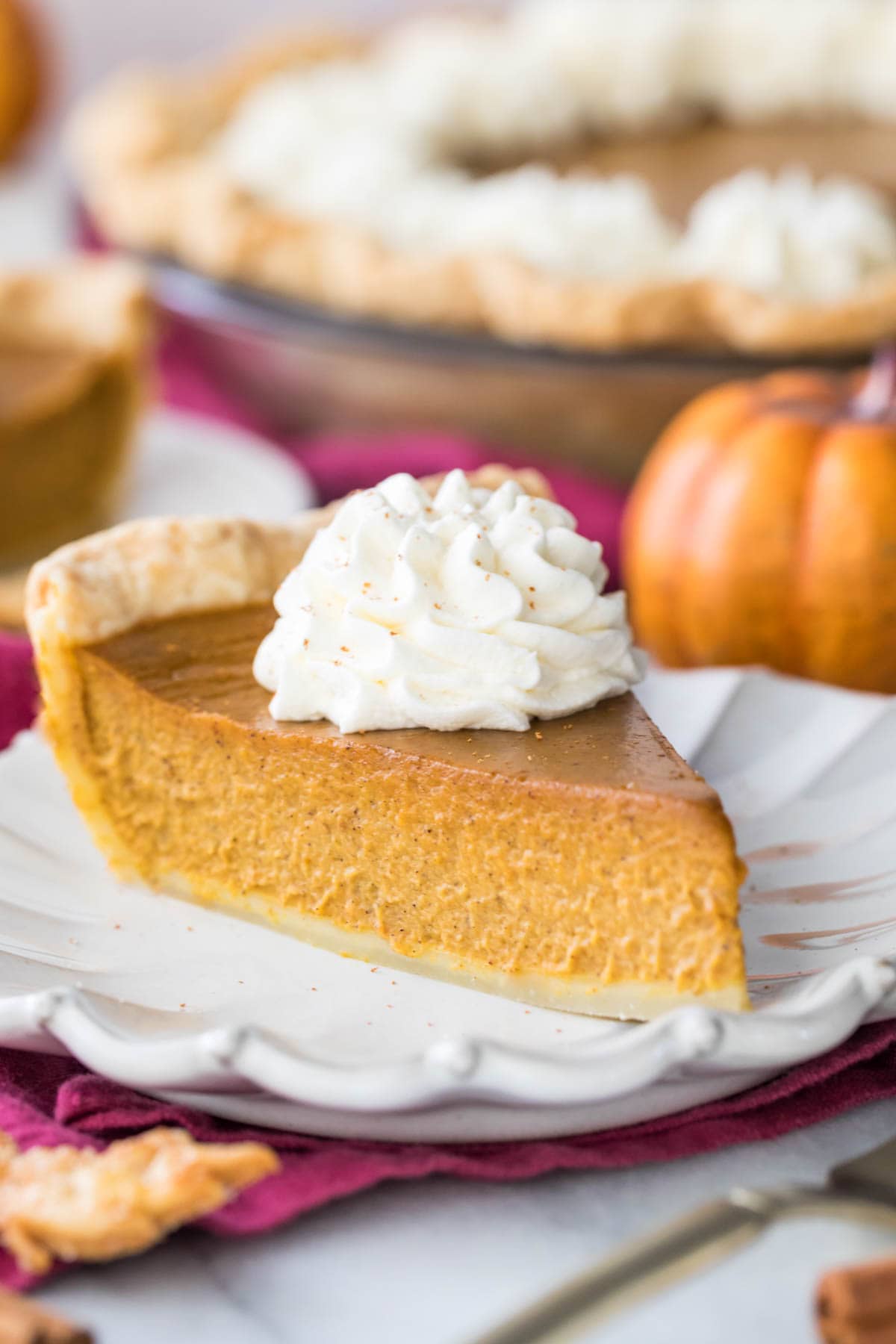 slice of pumpkin pie on white plate with remaining pie in the background