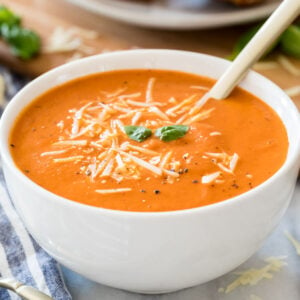 white bowl of hearty homemade tomato soup garnished with parmesan cheese, fresh basil, and cracked black pepper