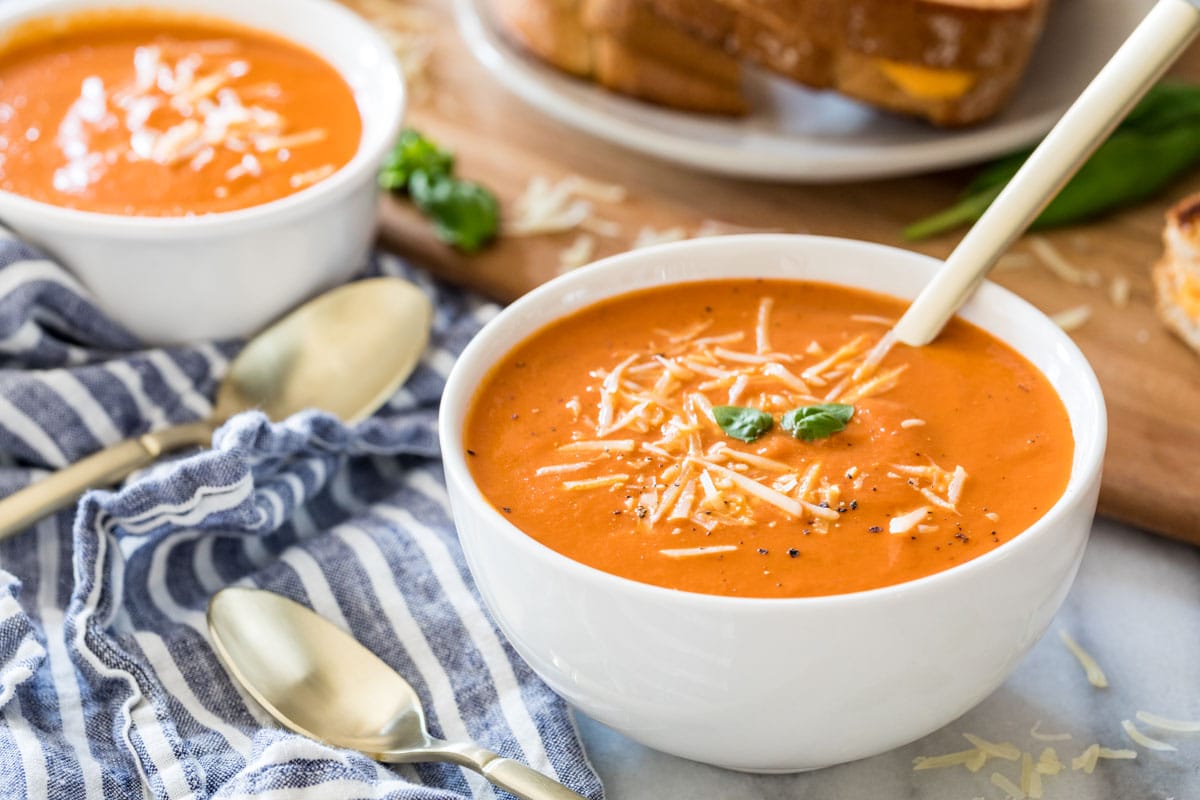bowls of creamy tomato soup topped with parmesan, fresh basil, and black pepper