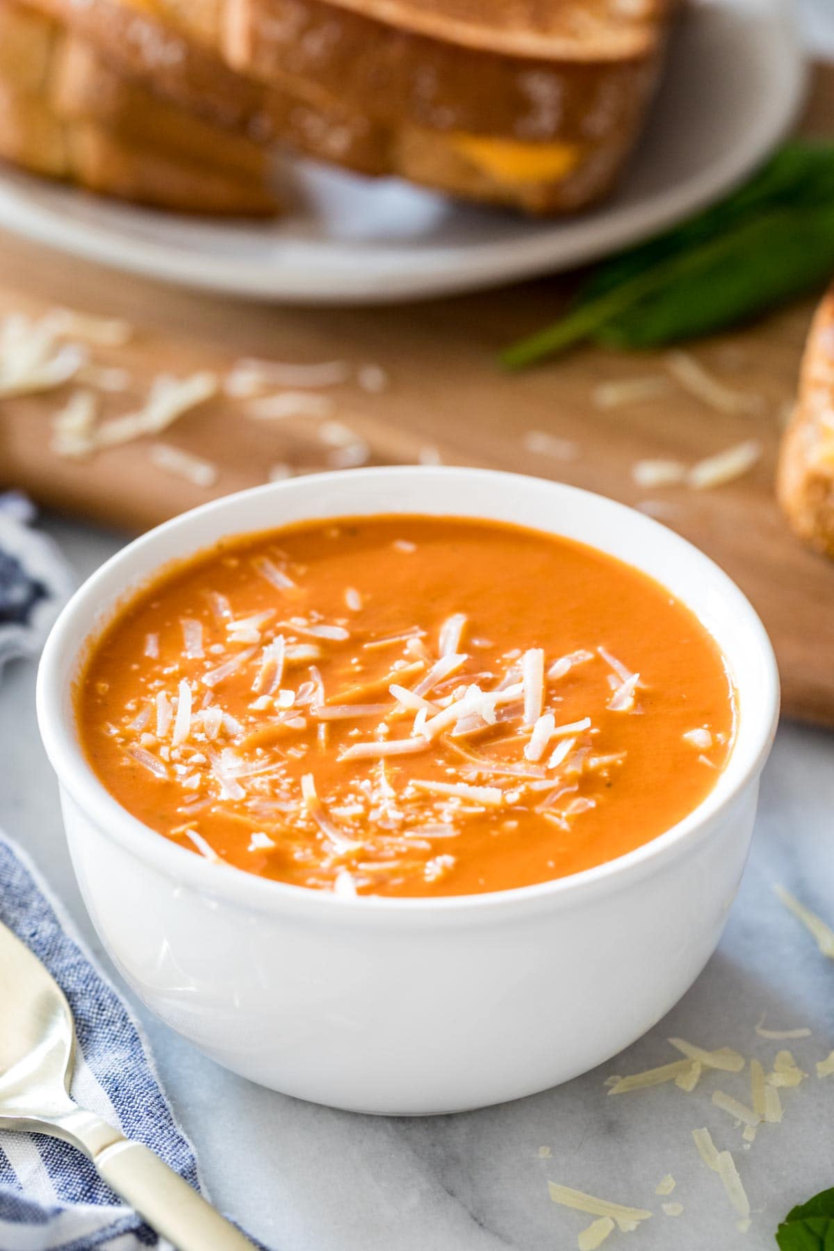 bowl of tomato soup in foreground with plate of grilled cheese sandwiches in background