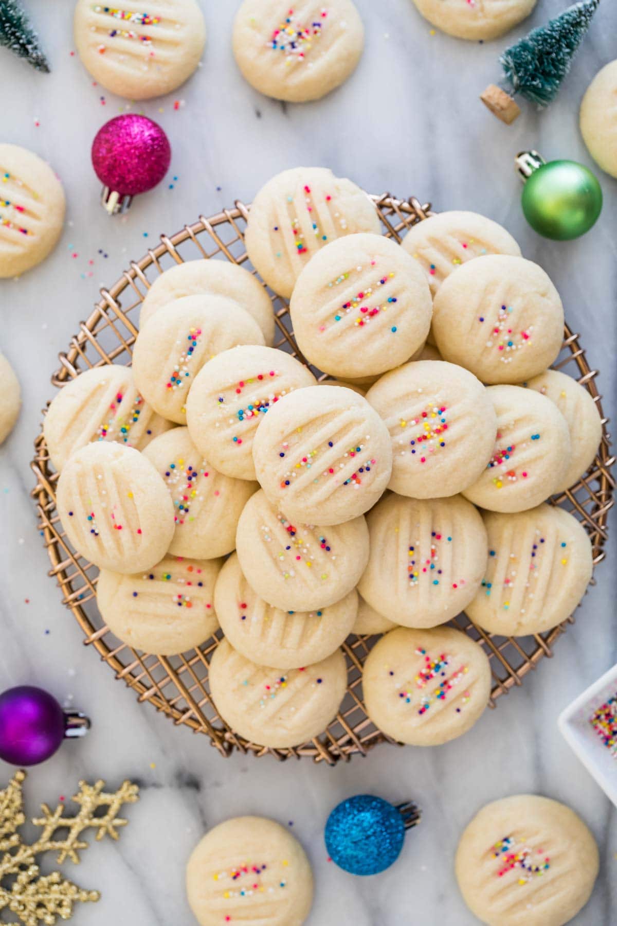 pile of whipped shortbread cookies with sprinkles on gold cooling rack