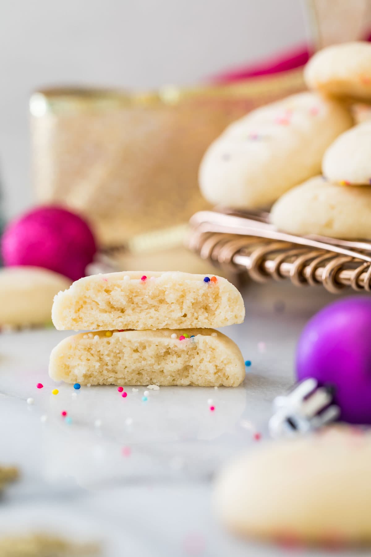 two halves of whipped shortbread cookies stacked on top of each other with Christmas ornaments in the background and foreground