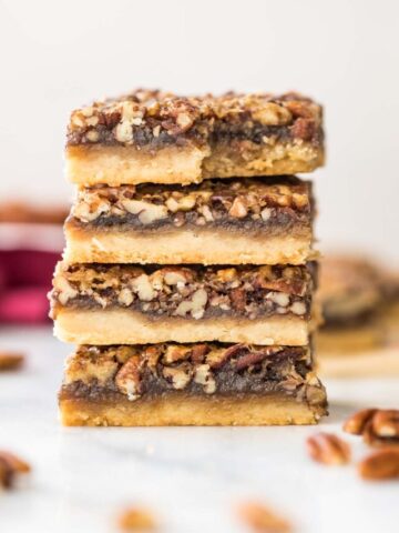 four pecan pie bars stacked on top of each other, with the top bar missing one bite