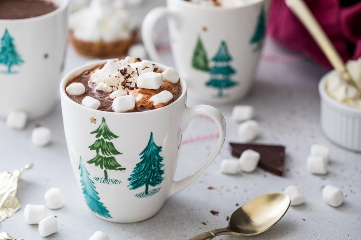 White mugs with evergreen trees filled with hot chocolate and marshmallows