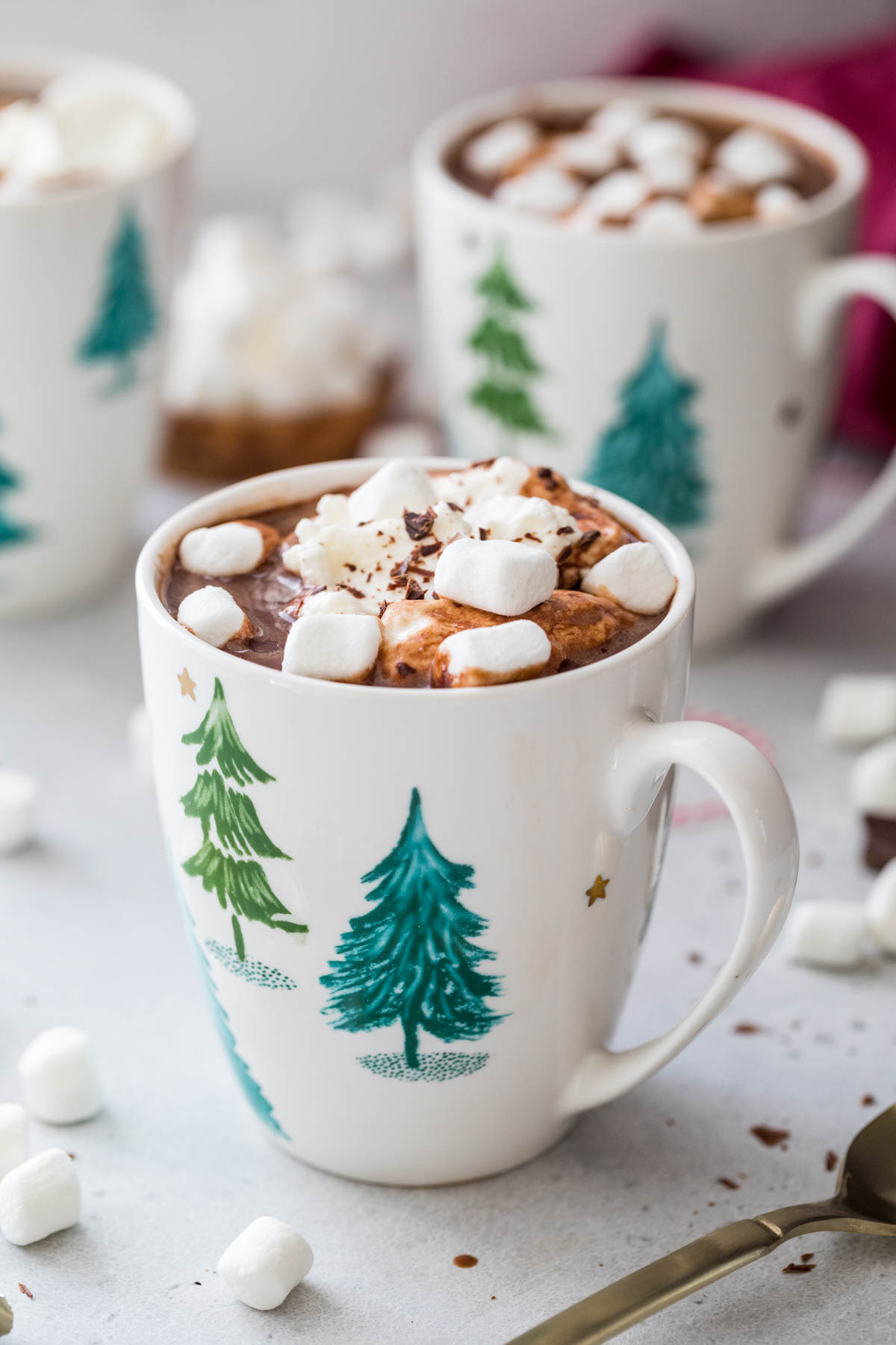 white mugs filled to the brim with hot chocolate topped with whipped cream, marshmallows, and chocolate shavings